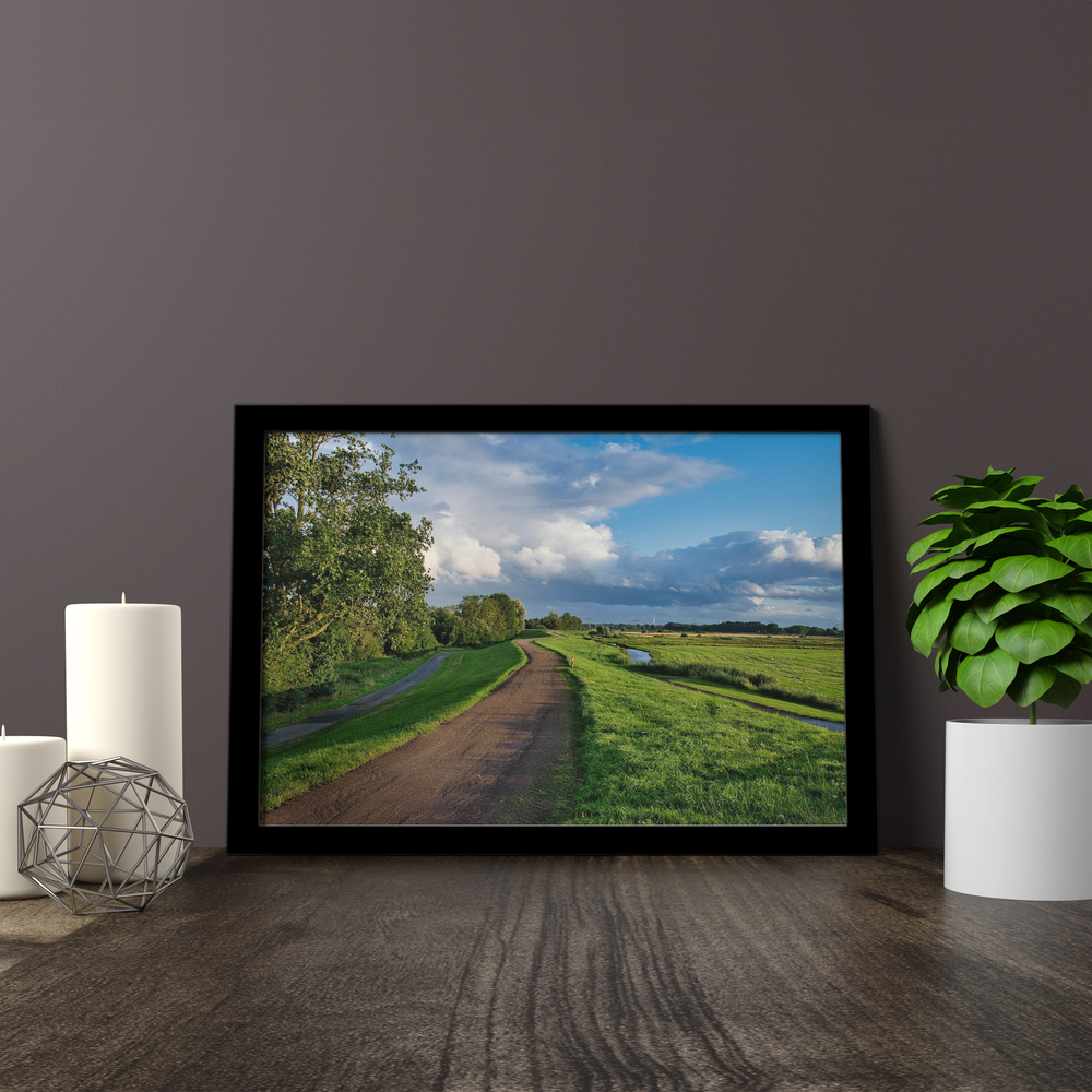 Photo de paysage sur plexiglas, cadre noir posé sur une surface en bois près de bougies et d’une plante