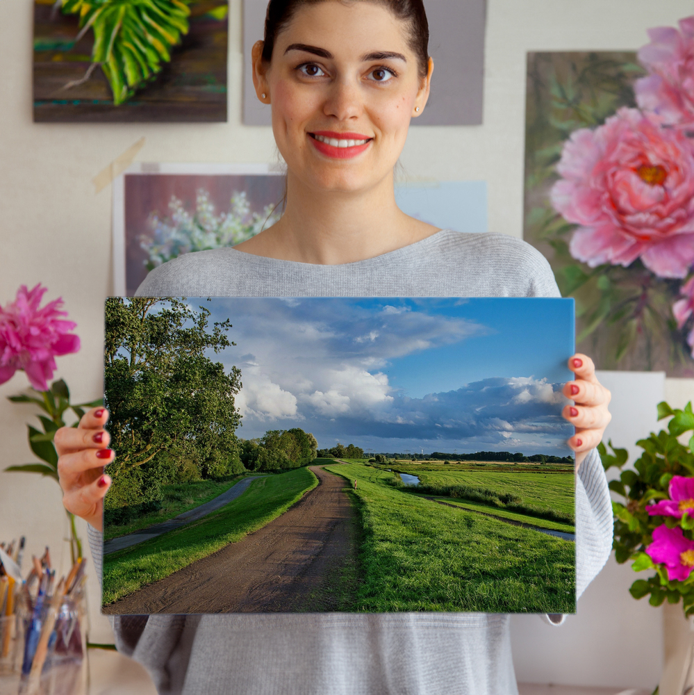 Photo sur plexiglas sans cadre avec chemin rural, prairies et ciel nuageux, devant des tableaux de fleurs