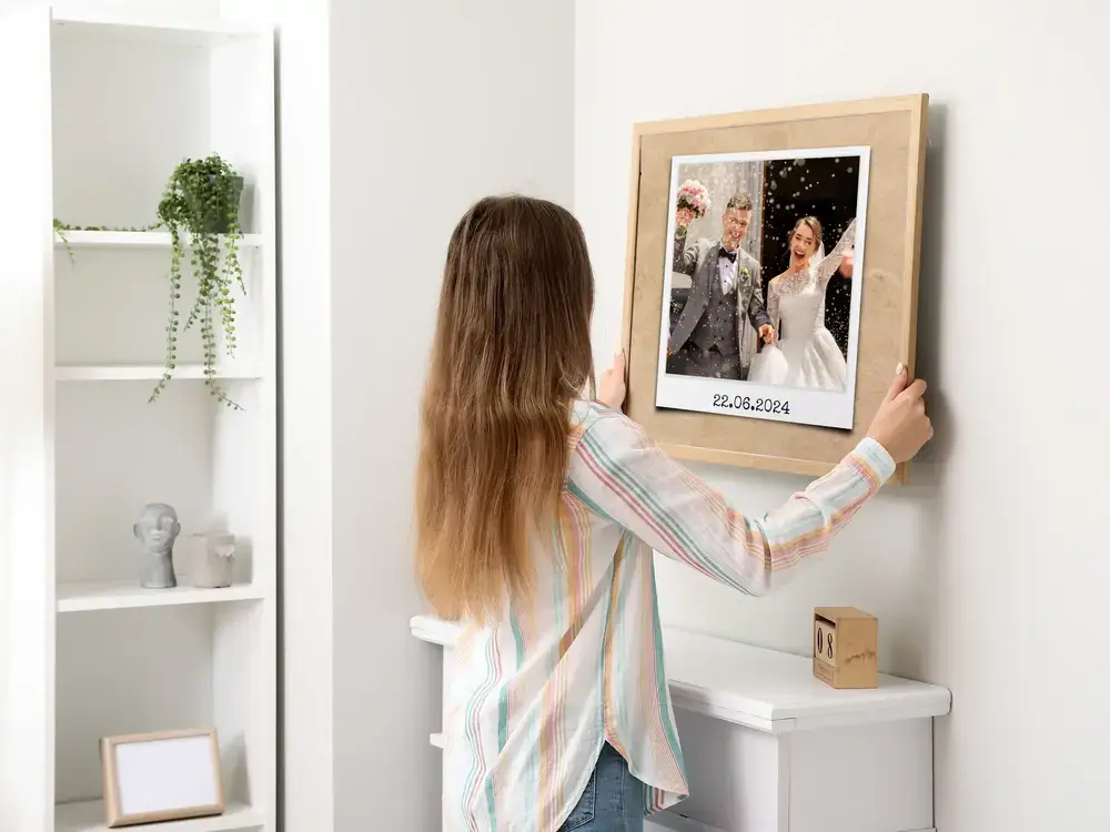 Photo de mariage datée dans un cadre en bois clair au mur blanc, un cadeau personnalisé pour les mariés