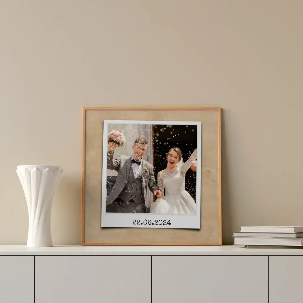 Photo de mariage façon instantané avec date, encadrée sur un buffet blanc à côté d’un vase