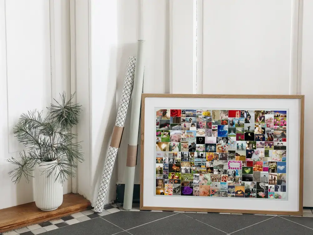 Collage de mariage aux nombreuses photos de tailles variées, dans un cadre en bois naturel posé au sol près d’une plante